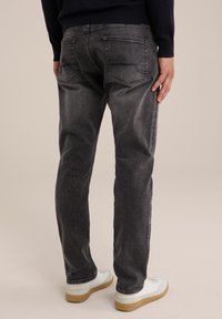 Jeans da uomo in denim grigio scuro con una vestibilità rilassata, dotati di cinque tasche, leggere sfumature e cuciture a contrasto sulle tasche posteriori.