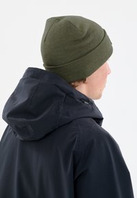Marineblaues Jacket mit einer weichen, strukturierten Oberfläche und Kapuze, kombiniert mit einer eng anliegenden, olivgrünen Strickmütze.