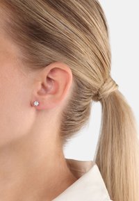 Silverfärgade studs med en blommotiv, som har klara stenar som accent. Glänsande yta med högpolerad finish.