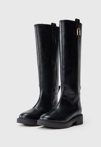 Bottes noires en cuir montantes avec une fermeture éclair sur le côté, bout rond, talon carré et un accent décoratif en or sur la boucle supérieure.