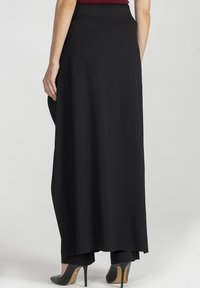 Czarna maxi spódnica o gładkiej fakturze, z dopasowanym paskiem w talii i plisami, zestawiona z czarnymi szpilkami, prezentująca czyste linie i minimalistyczny design.