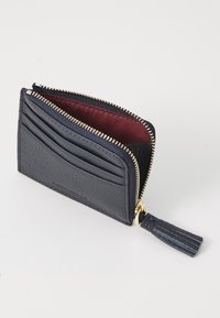 Carteira de couro azul-marinho com fecho de zíper, apresentando slots para cartões de um lado e um interior em bordô. Inclui um detalhe de tassel.