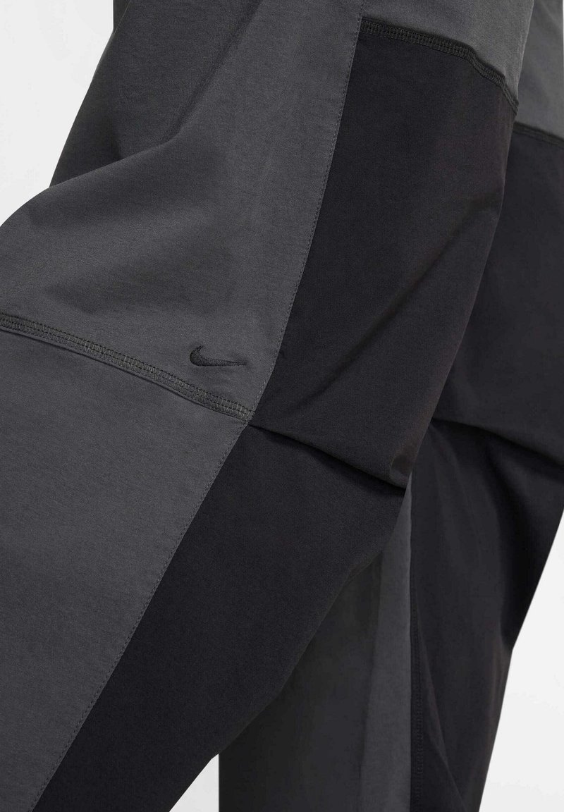 Pantalones deportivos negros y grises que presentan una tela texturizada, un logo de Nike y diseños de paneles en contraste para una apariencia moderna.