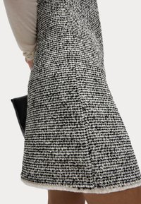 Vävd svart och vit texturerad kjol med en något trasig nederkant, som visar en strukturerad form och minimalistisk design.