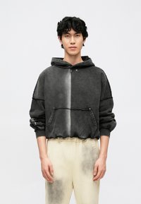 Sweatshirt com capuz em gradiente preto e cinza, com bolso canguru, capuz com cordão e punhos canelados. Ajuste descontraído com detalhes de bainha desfiada.