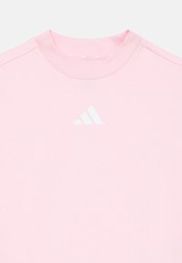 T-shirt en coton rose avec un col rond côtelé et un logo Adidas blanc sur la poitrine. Texture lisse avec des manches courtes.