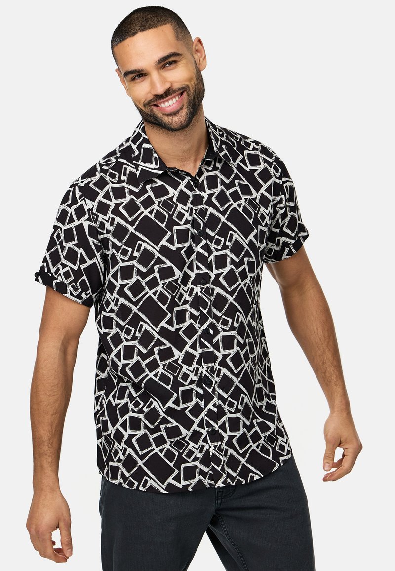 Chemise à manches courtes noire avec un motif géométrique contrastant blanc, dotée d'un col boutonné et d'une coupe décontractée.