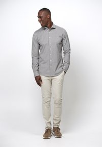Camicia grigia a maniche lunghe con bottoni, pantaloni slim-fit crema e sneakers in suede marrone. Tessuto liscio, colletto classico e bottoni frontali.