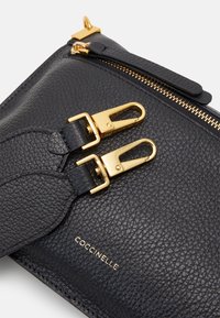 Borsa in pelle nera con texture, dotata di hardware dorato, doppi ganci e chiusura con zip. Il logo è impresso sulla parte anteriore inferiore.