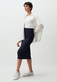 Camicia bianca a maniche lunghe sopra un top bianco a coste aderente, abbinata a una gonna blu navy fino al ginocchio e scarpe da ginnastica bianche. Tessuto morbido e design minimalista.