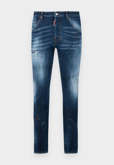 Donkerblauwe denim jeans met een smalle pasvorm, voorzien van een verweerd effect, subtiele vervaging en verfspatten in rood en wit.