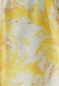 Geel en wit textiel met een zachte textuur, voorzien van een gemarmerd patroon met tinten oranje en een vloeiend ontwerp.