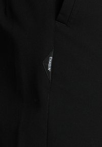 Schwarze Stoffhosen mit glatter Textur. Sie verfügen über ein markantes dreieckiges Markenpatch mit der Aufschrift "CHASIN'", das das Designdetail hervorhebt.