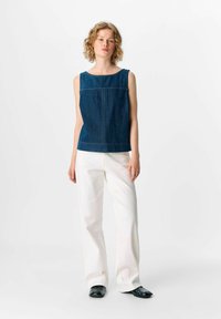 Mörkblå denimärmlös topp med rund halsringning och kontrasterande vit sömnad, matchad med vita vida byxor och svarta skor.