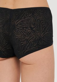 Boxers hipster pretos com um padrão texturizado que se assemelha a espirais. Feitos de um tecido leve e transparente, com uma cintura suave.