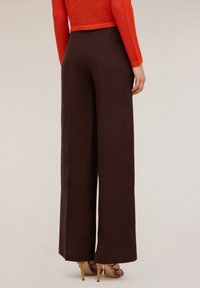 Pantaloni a gamba larga marroni realizzati in tessuto leggero, caratterizzati da una texture liscia, con una vita alta e dettagli di cucitura discreti.