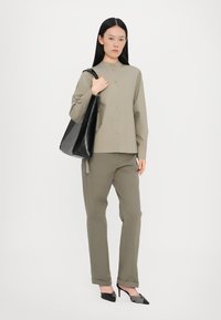 Olive green button-up shirt with long sleeves, paired with matching trousers and black leather shoulder bag. Pointed black heels.