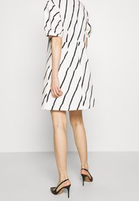 Valkoinen mekko, jossa on mustia vinoja raitoja, lyhyet puffihihat, vetoketjukiinnitys takana. Yhdistetty mustiin avokkaisiin. Sileä kangas.