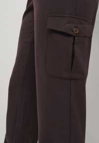 Pantalons cargo marron foncé avec une poche latérale, dotés d'une fermeture à bouton. Fabriqués à partir d'un tissu lisse avec une coupe ajustée et des lignes épurées.