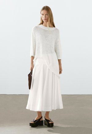 Maglione bianco di maglia oversize abbinato a una lunga gonna bianca fluente e sandali con piattaforma neri. Accessorio: borsa intrecciata marrone.