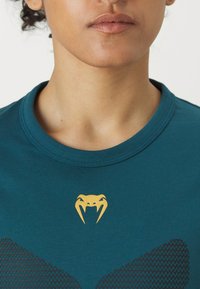 Sile t-särk, mis on valmistatud siledast kangast, millel on rindkerel kollane mao logo ja allosas tekstureeritud must muster. Ümar kaelus.