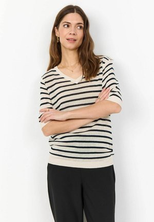Pull en V en crème avec des rayures horizontales bleu marine. Manches courtes, ourlet et poignets côtelés, avec une texture lisse. Associé à un pantalon noir.