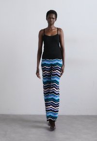 Black sleeveless top paired with multicolored wave-patterned pants in blue, black, and white. Model stands against a plain background.