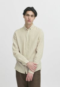 Lys beige knapp-up skjorte med vertikale striper, med lange ermer, en spiss krage, og en litt buet nederkant.