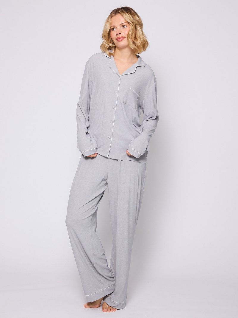 Conjunto de pijama gris claro con una camisa de botón que presenta un bolsillo y mangas largas. Los pantalones son de corte holgado con un dobladillo sencillo. Textura de tela suave.