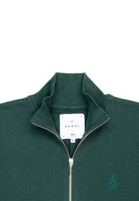 Sudadera con cremallera en verde oscuro, con cuello acanalado, logo bordado en el lado izquierdo del pecho y una etiqueta que muestra "EDWIN" talla M en el interior.