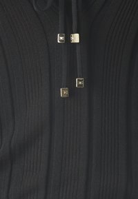 Schwarzer, gerippter Pullover mit Reißverschluss vorn, metallischen quadratischen Beschlägen und Kordelzügen, die ein strukturiertes und texturiertes Erscheinungsbild schaffen.