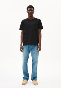 Zwarte katoenen t-shirt met een borstzak, gecombineerd met lichtblauwe spijkerbroek en beige instapschoenen. Eenvoudige, casual pasvorm.