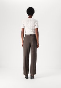 Pull tricot blanc à manches courtes avec motif torsadé, associé à un pantalon marron taille haute doté d'une poche arrière et de passants de ceinture minces.