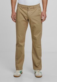 Chinos din bumbac bej, cu un design drept, dotate cu fermoar frontal, închidere cu nasture și buzunare laterale. Asortați cu adidași albi și verzi.