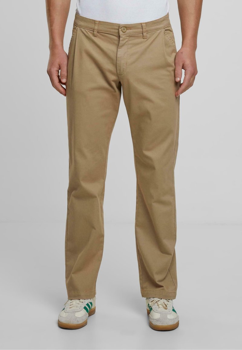Chinos din bumbac bej, cu un design drept, dotate cu fermoar frontal, închidere cu nasture și buzunare laterale. Asortați cu adidași albi și verzi.