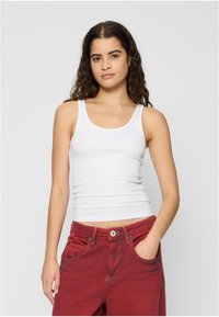 Hvit bomulls tank topp med scoop hals og smale skulderstropper, kombinert med dype røde høyhalsede jeans med lommer.