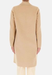 Cappotto di lana beige, lungo fino al ginocchio, con un colletto semplice, maniche lunghe e una linea dritta caratterizzata da dettagli di cucitura minimalisti.
