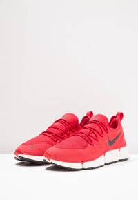 Röda sneakers gjorda av nät och syntetiska material med en svart Nike-logotyp, tjock vit mellansula och texturerad gummiyttersula.