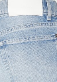 Vaaleansiniset farkut, joissa on takatasku, valkoinen nahkainen etiketti kuviotekstillä ja näkyvät ompelusaumat.