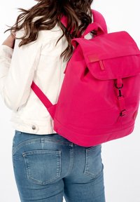 Světlý růžový batoh s klopovým zavíráním, nastavitelné popruhy a černým detaily na přezce, vyrobený z odolného materiálu.