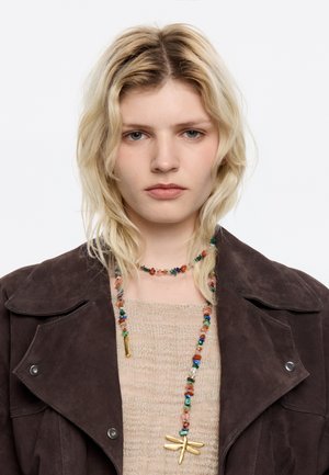 Chocolate brown suede jacket over a beige sweater, featuring a multicolored bead necklace with a gold dragonfly pendant.