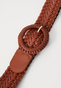 Woven leather belt in dark brown with a circular buckle, featuring a braided design and a smooth rectangular leather tag.
