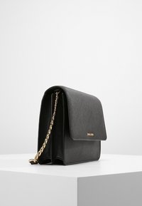 Schwarze strukturierte Handtasche aus strukturiertem Material, mit einem Kettegurt in Goldtönen und einem Klappenverschluss, sowie einem dezenten Logo auf der Vorderseite.