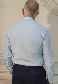 Chemise de dress en rayures bleu clair avec un col structuré, des manches longues et une coupe ajustée, associée à un pantalon à rayures foncées.