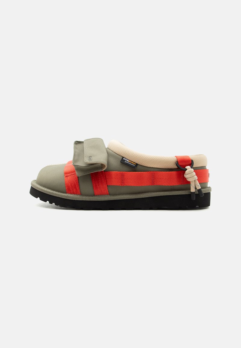 Sandale mule vert olive clair avec lanières rouges, col rembourré beige, semelle noire et détail de rabat avant ajustable sur fond blanc.
