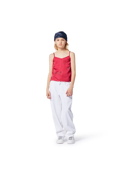Rode satijnen top met dunne bandjes, voorzien van zilveren letters en grafische ontwerpen, gecombineerd met losse witte broek en sneakers.