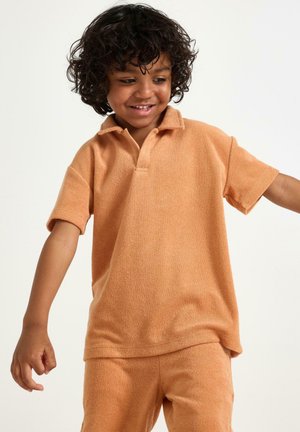 Kortärmad polotröja i mjuk, strukturerad orange tyg med krage. Kombinerad med matchande shorts, designade för komfort.