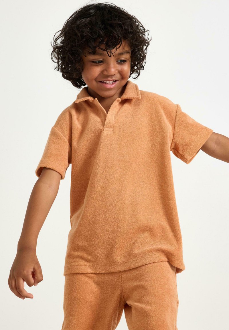 Kortærmet polo skjorte i blødt, struktureret orange stof med krave. Kombineret med matchende shorts, designet til komfort.
