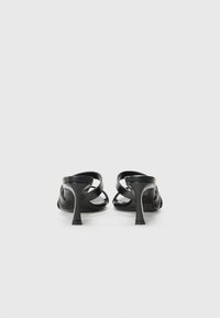 Sandales à talons hauts noires avec un design épuré, présentant des brides croisées et une finition texturée sur le dessus. Talon surélevé, esthétique minimaliste.