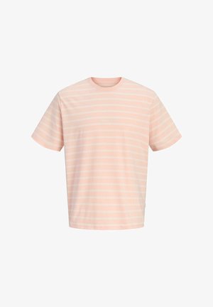 Lyshåret dreng stående iført en pinkstribet T-shirt, blå denimshorts, hvide sokker og beige sneakers på en ensfarvet lys baggrund.